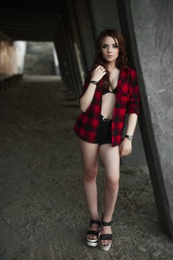 Poz ve kentsel duvar arka planda kırmızı kareli gömlek, şort, açık havada yaz portre yakınındaki gülümseyen güzel genç hippi kız.