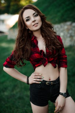 Poz ve kentsel duvar arka planda kırmızı kareli gömlek, şort, açık havada yaz portre yakınındaki gülümseyen güzel genç hippi kız.