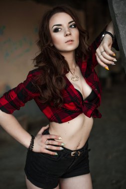 Poz ve kentsel duvar arka planda kırmızı kareli gömlek, şort, açık havada yaz portre yakınındaki gülümseyen güzel genç hippi kız.