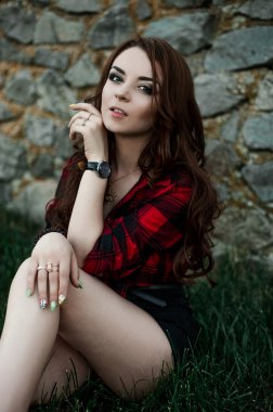 Poz ve kentsel duvar arka planda kırmızı kareli gömlek, şort, açık havada yaz portre yakınındaki gülümseyen güzel genç hippi kız.