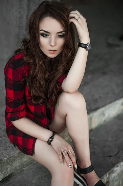 Hermosa chica hipster joven posando y sonriendo cerca de fondo de pared urbana en camisa a cuadros rojo, pantalones cortos, al aire libre retrato de verano . — Foto de Stock