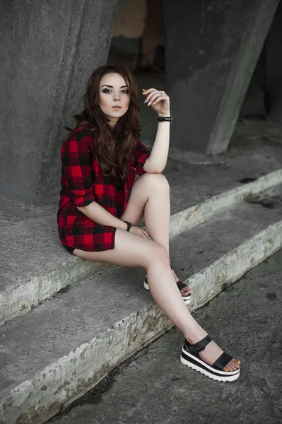 Menina bonita hipster posando e sorrindo perto de fundo da parede urbana em camisa xadrez vermelho, shorts, ao ar livre retrato de verão . — Fotografia de Stock