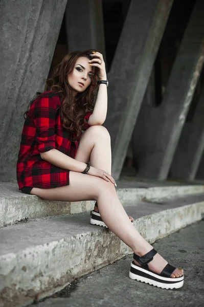 美丽的年轻时髦女孩摆姿势和附近城市的墙背景的红色格子衬衫、 短裤、 户外夏天肖像微笑. — 图库照片