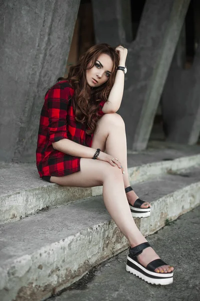 美丽的年轻时髦女孩摆姿势和附近城市的墙背景的红色格子衬衫、 短裤、 户外夏天肖像微笑. — 图库照片