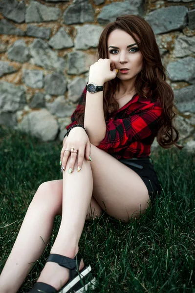 Menina bonita hipster posando e sorrindo perto de fundo da parede urbana em camisa xadrez vermelho, shorts, ao ar livre retrato de verão . — Fotografia de Stock
