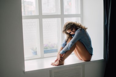 Pencerede oturuyor ve dışında arayan genç güzel kadın mavi tişört giyiyor geri kalanı, sahiptir. Stüdyo düzeltisiz atış.