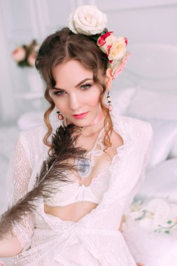 Beyaz dantel elbise, saç çiçeklerle süslenmiş beyaz yatak, güzel genç seksi kadın oturuyordu. Mükemmel makyaj. Güzellik moda. Kirpik. Stüdyo düzeltisiz atış. 
