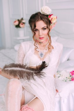 Beyaz dantel elbise, saç çiçeklerle süslenmiş beyaz yatak, güzel genç seksi kadın oturuyordu. Mükemmel makyaj. Güzellik moda. Kirpik. Stüdyo düzeltisiz atış. 
