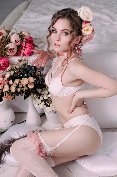 Mooie jonge sexy vrouw, het dragen van witte lingerie, kamer versierd met bloemen. Perfecte make-up. Beauty Beli parfum mode. Wimpers. Studio geretoucheerd schot. — Stockfoto