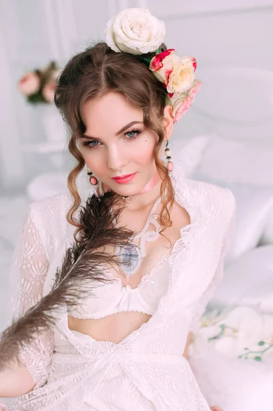 Beyaz dantel elbise, saç çiçeklerle süslenmiş beyaz yatak, güzel genç seksi kadın oturuyordu. Mükemmel makyaj. Güzellik moda. Kirpik. Stüdyo düzeltisiz atış. 