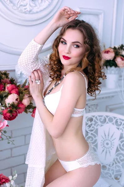 Beautiful young sexy woman , wearing white lingerie, room decorated with flowers. Perfect makeup. Beauty fashion. Eyelashes. Studio retouched shot.