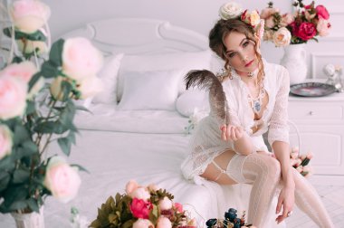 Beyaz dantel elbise, saç çiçeklerle süslenmiş beyaz yatak, güzel genç seksi kadın oturuyordu. Mükemmel makyaj. Güzellik moda. Kirpik. Stüdyo düzeltisiz atış. 