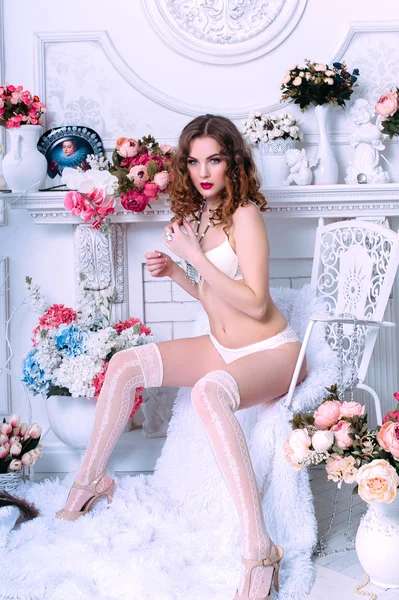 Mooie jonge sexy vrouw, het dragen van witte lingerie, kamer versierd met bloemen. Perfecte make-up. Beauty Beli parfum mode. Wimpers. Studio geretoucheerd schot. — Stockfoto
