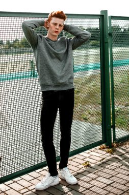 Casual giyim güneşli bir günde açık, stadium yanında duran bir genç yakışıklı kırmızı saçlı moda çocuk