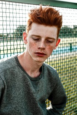 Casual giyim güneşli bir günde açık, stadium yanında duran bir genç yakışıklı kırmızı saçlı moda çocuk. Yakın, düzeltisiz atış.