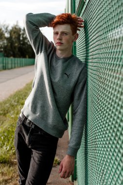 Casual giyim güneşli bir günde açık, stadium yanında duran bir genç yakışıklı kırmızı saçlı moda çocuk