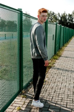 Casual giyim güneşli bir günde açık, stadium yanında duran bir genç yakışıklı kırmızı saçlı moda çocuk