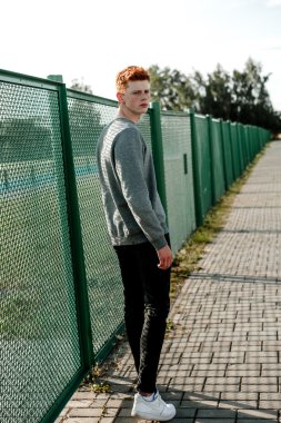 Casual giyim güneşli bir günde açık, stadium yanında duran bir genç yakışıklı kırmızı saçlı moda çocuk