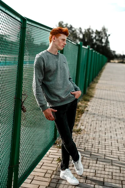 One young handsome red haired fashionable boy standing near stadium in sunny day outdoor , wearing casual clothing — Stock Photo, Image