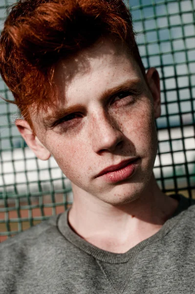 One young handsome red haired fashionable boy standing near stadium in sunny day outdoor , wearing casual clothing — Stock Photo, Image