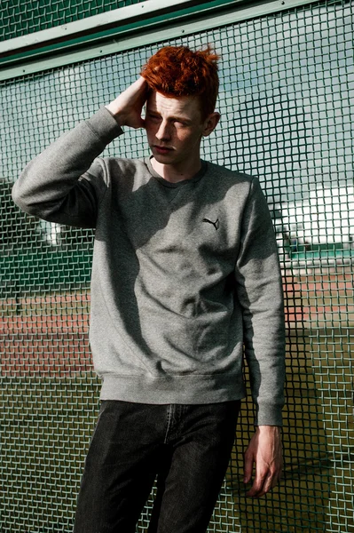 One young handsome red haired fashionable boy standing near stadium in sunny day outdoor , wearing casual clothing — Stock Photo, Image