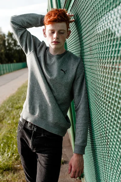 En ung vacker röda haired fashionabla pojke står nära stadium i solig dag utomhus, bär casual kläder — Stockfoto