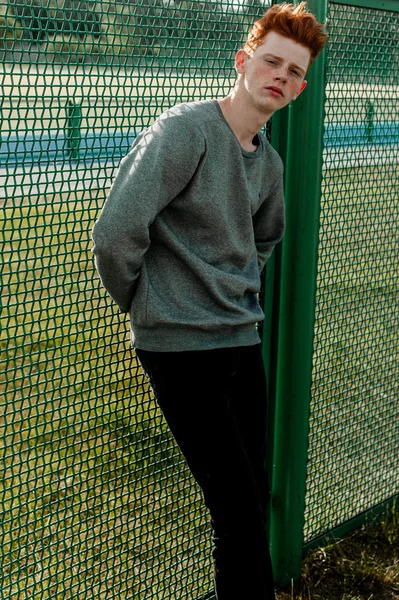 En ung vacker röda haired fashionabla pojke står nära stadium i solig dag utomhus, bär casual kläder — Stockfoto