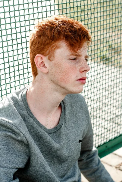 One young handsome red haired fashionable boy standing near stadium in sunny day outdoor , wearing casual clothing — Stock Photo, Image