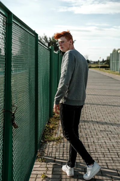 One young handsome red haired fashionable boy standing near stadium in sunny day outdoor , wearing casual clothing — Stock Photo, Image