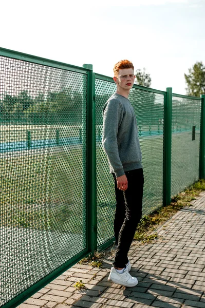 한 젊은 잘생긴 빨간 머리 유행 소년 화창한 날 야외, 경기장 근처 서 캐주얼 옷을 입고 — 스톡 사진