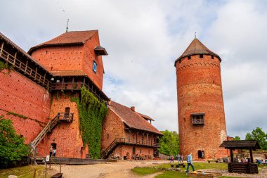 Turaida kalesi yeşil ağaçlar ve bulutlu gökyüzü ile çevrili.