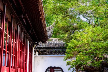 Yuyuan Bahçeleri 'ndeki yeşil ağaçların yanındaki kırmızı ahşap bina.