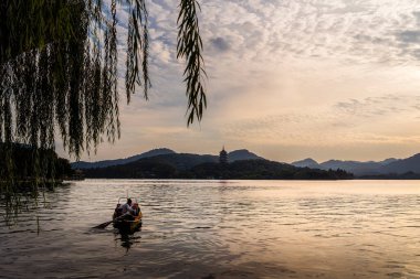 İnsanlar Hangzhou 'da gün batımında Batı Gölü' nde kayıkla geziyorlar.
