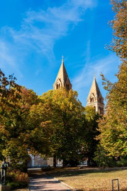 Renkli sonbahar ağaçlarıyla çevrili uzun kilise kuleleri.