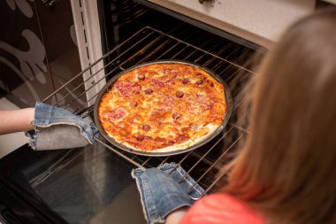 Kadın elinin fırından hazır pizzayı çıkardığı en iyi manzara. Evde yemek pişirmek. Düşük Dof.