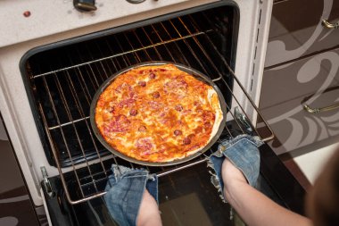 Kadın elinin fırından hazır pizzayı çıkardığı en iyi manzara. Evde yemek pişirmek. Düşük Dof.