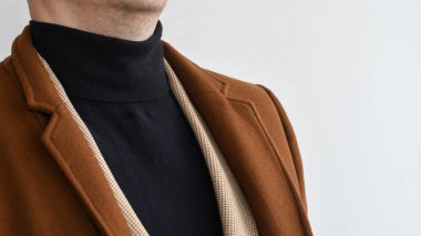 Erkek üstünlüğü, şık erkek kahverengi paltosu, siyah kazak ve bej ceket. Seçici odak.