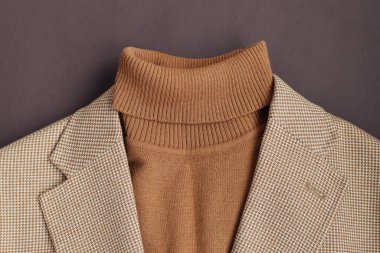 Erkekler düz giyinir yakın plan, şık erkek kahverengi kazağı açık bej ceketle koyu kahverengi arka plan. 