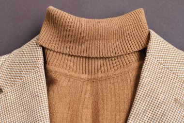 Erkekler düz giyinir yakın plan, şık erkek kahverengi kazağı açık bej ceketle koyu kahverengi arka plan. 