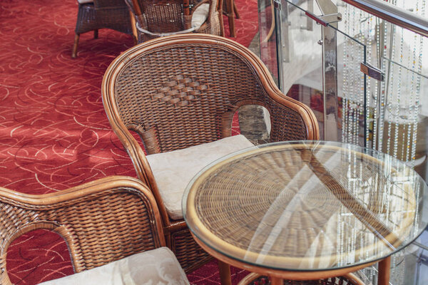 Detail of rattan chairs outdoors and tea table in hotel interior. Selective focus.