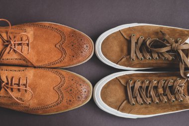 Bir çift şık kahverengi süet derbi ayakkabısı kahverengi arka planda bej spor ayakkabılara karşı, minimalizmi ve zarif stili vurguluyor. Üst görünüm.