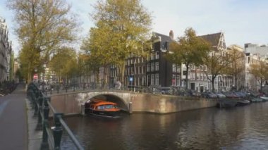 AMSTERDAM, NETHERLANDS-OCTOBER, 12, 2017: Amsterdam 'da bir kanal köprüsünün altından geçen turuncu tur teknesi