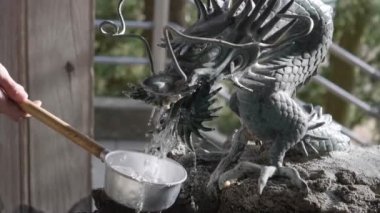 Arakura Sengen Tapınağı 'ndaki ejderha şekilli çeşmeden bir kepçeyi dolduran 180p yavaş çekim şarjörü.