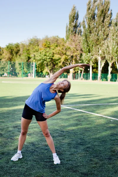 Kvinna stretching i fitness motion utanför genom park. Vacker passform kvinnlig fitness flicka modell på park gör stretch träning efter träning. Friska livsstil koncept — Stockfoto