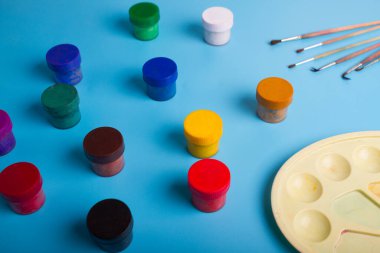 Mavi arka planda renkli boya kutuları ve fırçalar