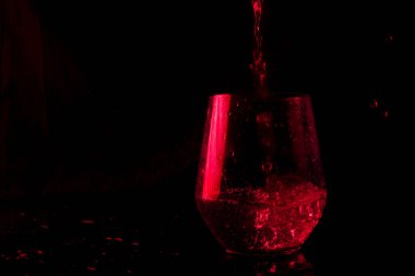 Mavi ve kırmızı renklerle işaretlenmiş su, siyah bir arkaplanda cam bir kadehe sıçrıyor.