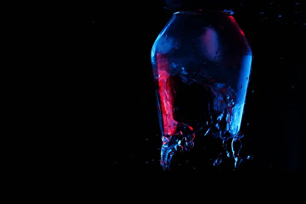 黒い背景にガラスのゴブレットに水が青と赤で強調表示されます — ストック写真