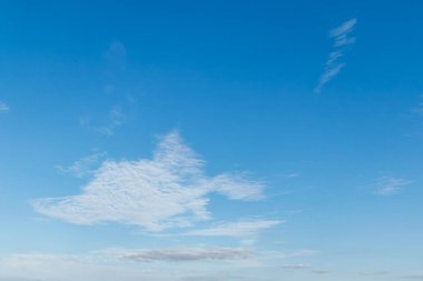 Parlak mavi gökyüzünün minimalist görüntüsü dağınık sirrus bulutları güneşli bir günde huzurlu ve havadar bir atmosfer yaratıyor..
