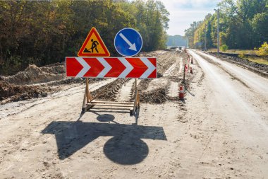 Toprak yol üzerindeki trafiği yönlendiren yol yapım uyarıları, orman kırsalındaki güvenlik önlemlerini ve altyapı bakımını gösteriyor.