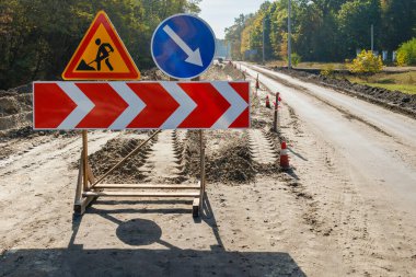 Toprak yol üzerindeki trafiği yönlendiren yol yapım uyarıları, orman kırsalındaki güvenlik önlemlerini ve altyapı bakımını gösteriyor.